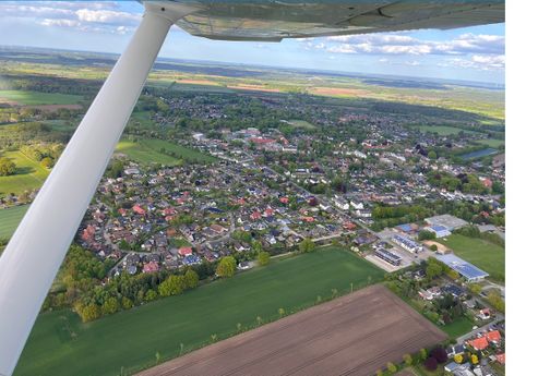 Luftaufnahme: ein Ort mit Wohngebiet, Feldern und Straßen, aufgenommen aus einem Kleinflugzeug.
