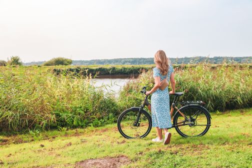 Eine Frau steht mit ihrem Fahrrad am Ufer der Stör und genießt den Blick in die Landschaft.