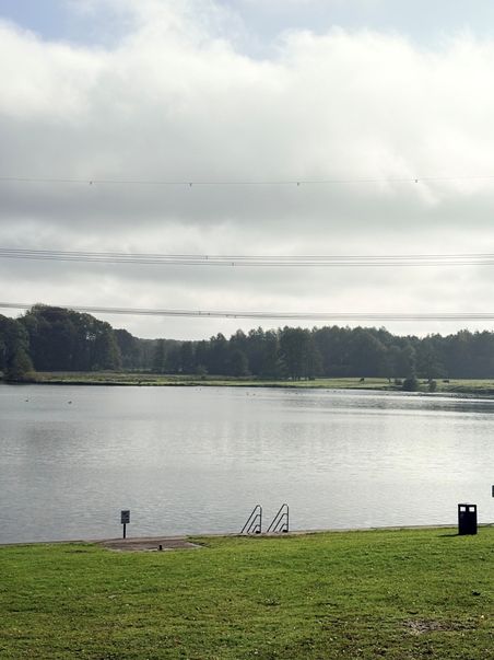  Naturbad Oberglinde mit Uferwiese, Einstiegstreppe und bewölktem Himmel.