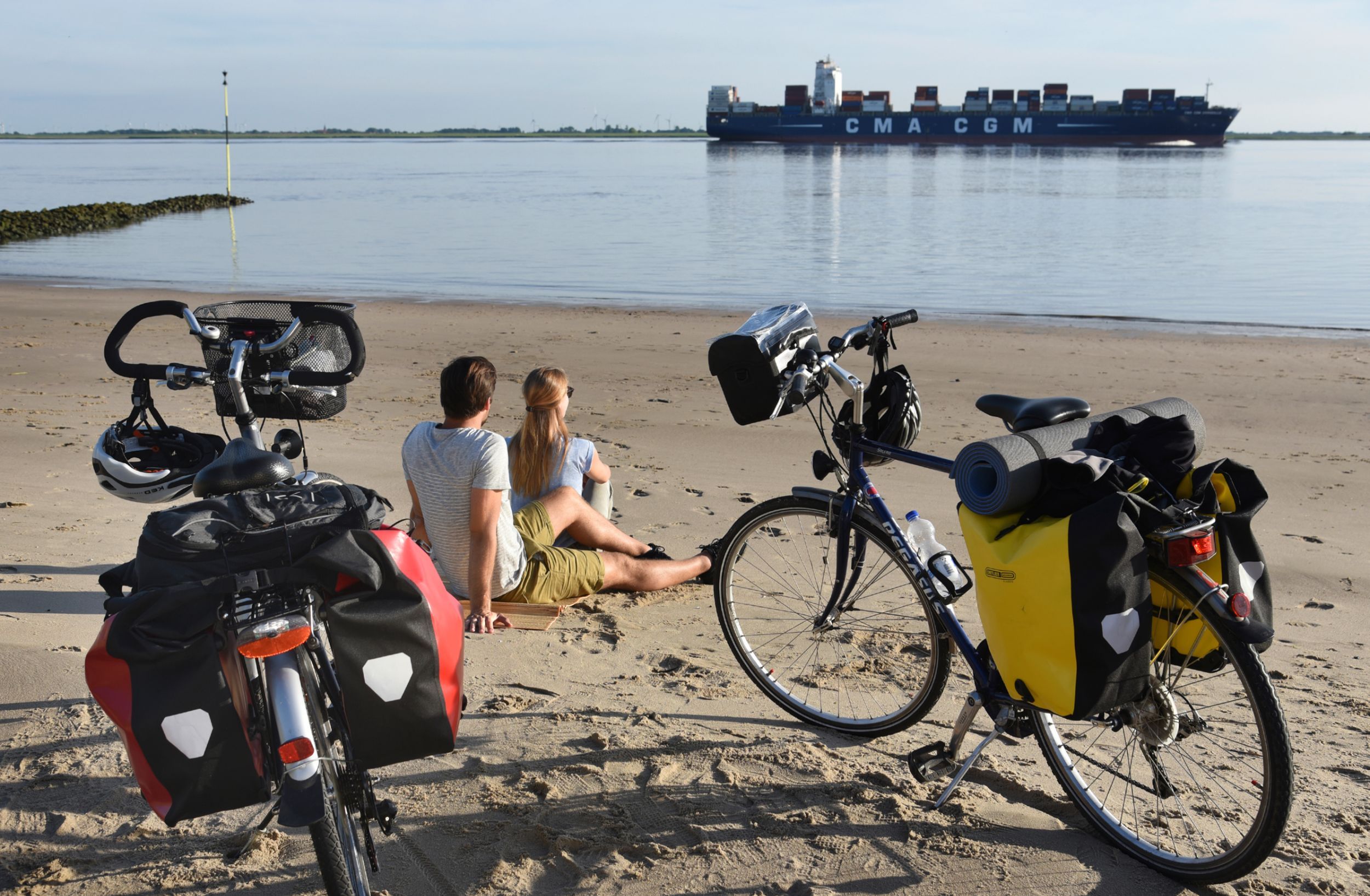 Paar ist mit dem Fahrrad auf dem Elberadweg unterwegs und genießt eine Pause am Elbstrand in Brokdorf und beobachtet die Schiffe.