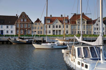 Segelboote im Hafen von Glückstadt vor einer Kulisse historischer Gebäude mit roten Ziegeldächern und verzierten Fassaden.