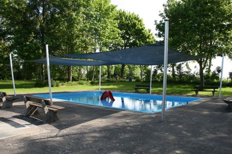 Babypool mit Sonnensegeln und roter Rutsche, umgeben von Bäumen und Bänken im Freien.