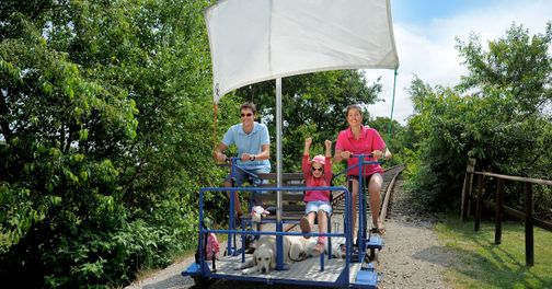 Familie auf der Marschenbahn-Draisine im Grünen, mit Hund an Bord.