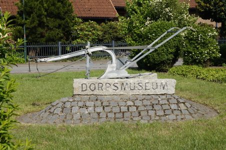 Metallpflug auf Steinsockel mit der Aufschrift „DORPSMUSEUM“ im Garten des Dorfmuseums Ottenbüttel.