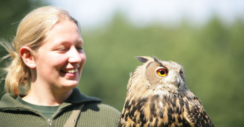 Im Wildpark Eekholt lächelt eine Frau neben einer Eule mit orangefarbenen Augen.