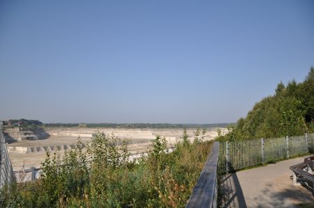 Aussichtspunkt mit Blick auf die Kreidegruben in Lägerdorf. Im Vordergrund sind Pflanzen und ein Zaun zu sehen, rechts ein Weg mit Sitzbank.