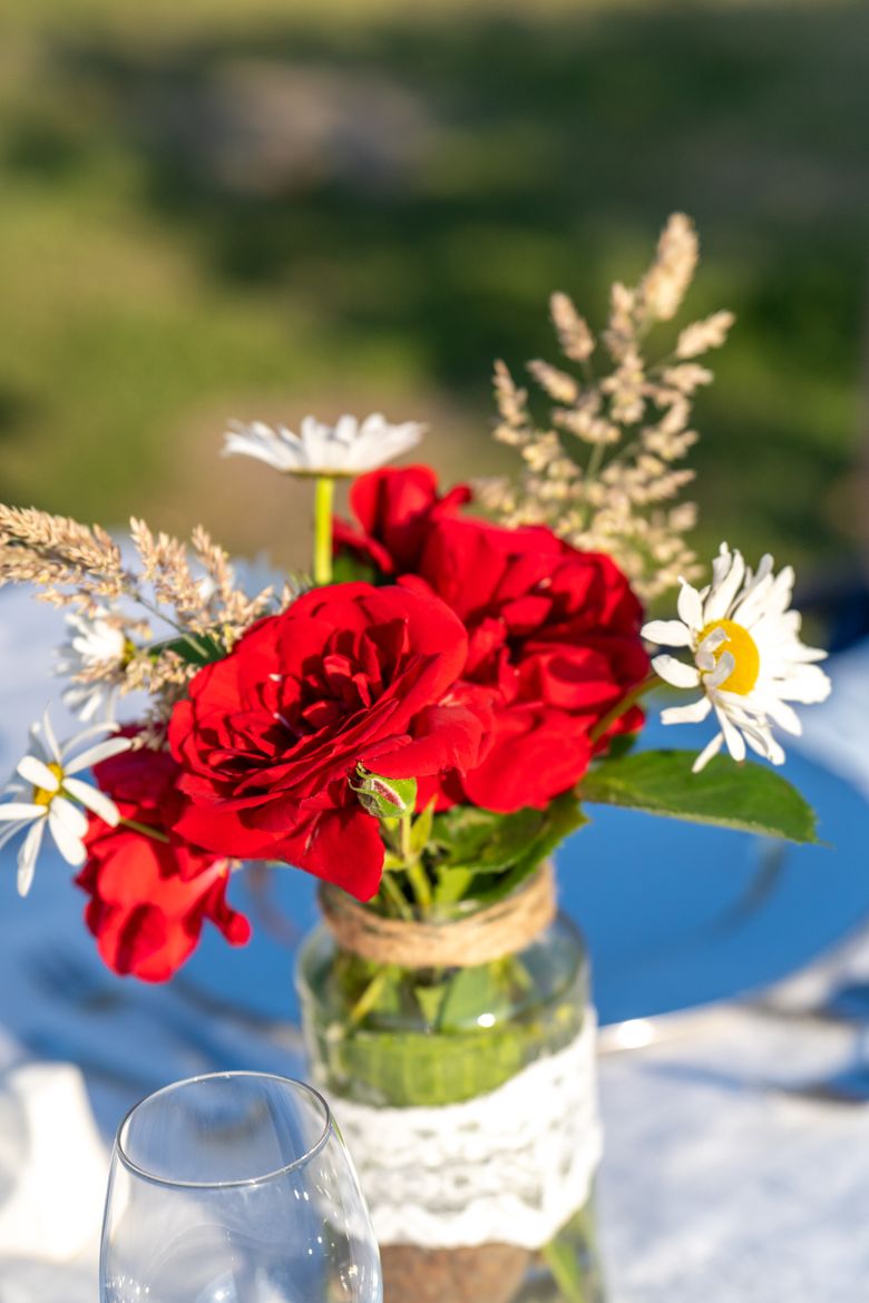 Rotes Blumenarrangement auf dem Tisch mit unscharfem Blick in die Natur.