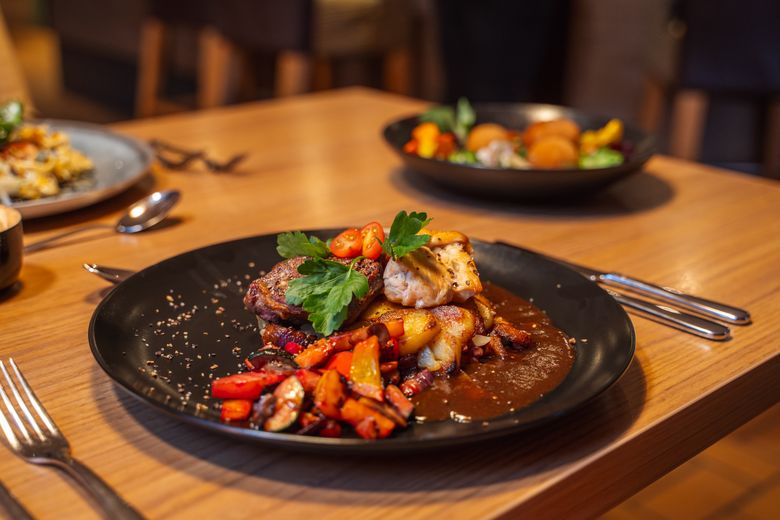 Ein kunstvoll angerichtetes Fleischgericht mit Gemüse und Soße auf einem schwarzen Teller, serviert auf einem Holztisch im Landgasthof Unter den Linden.