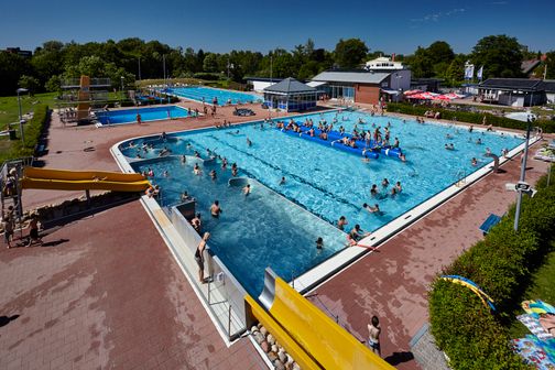 Roland-Oase mit Freibad, Rutschen, Schwimmbecken und vielen Badegästen bei Sonnenschein.