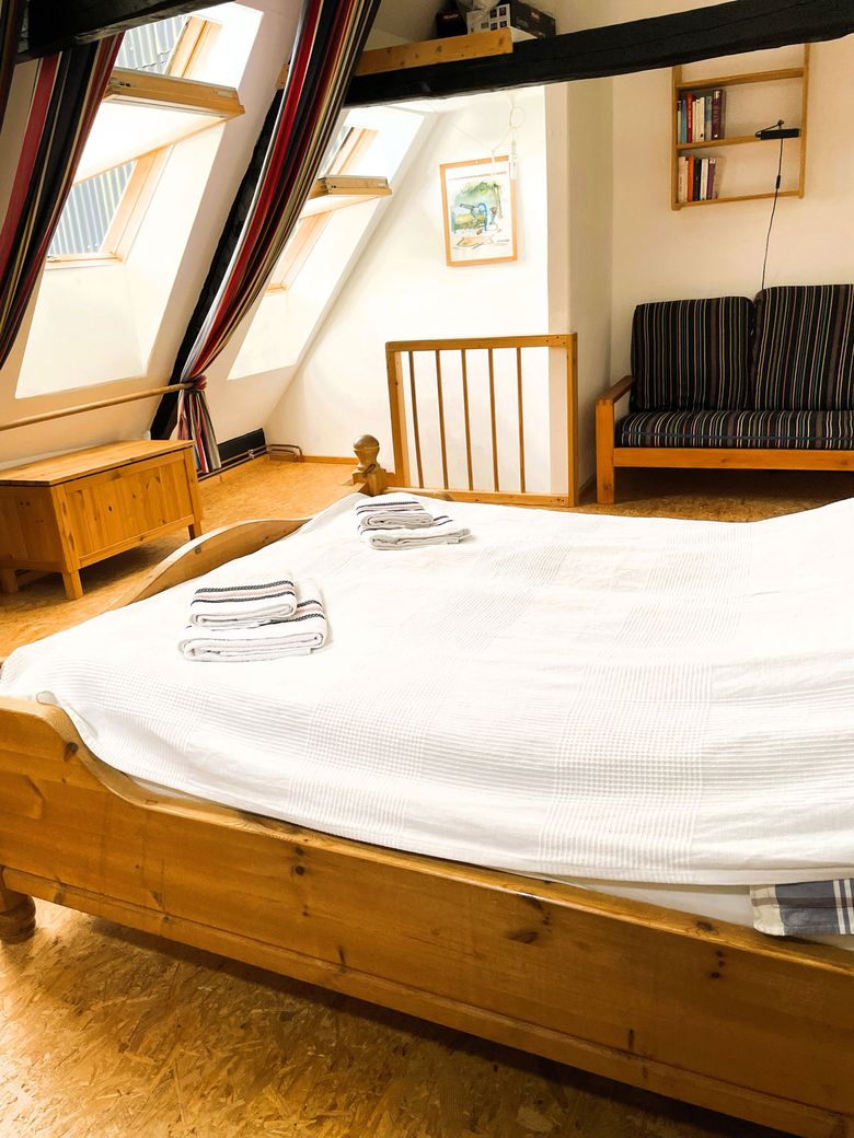 Gemütliches Dachgeschosszimmer mit Holzbett, Dachfenstern, Sofa und Bücherregal. Helle Atmosphäre durch einfallendes Licht.