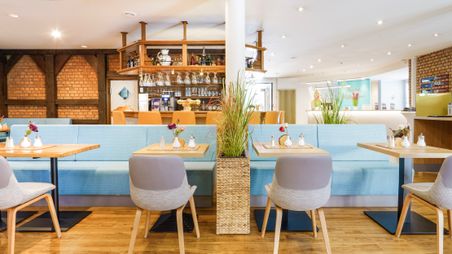 Frühstücksraum mit Tischen, Stühlen und Sitzbänken, mit Bar im Hintergund