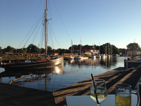 Ein idyllischer Hafen bei Sonnenuntergang mit Segelbooten und einem Tisch mit Getränken im Vordergrund.