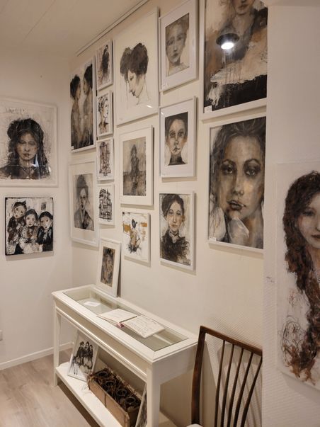 Atelier Lamade: kleiner Galerieraum mit zahlreichen gerahmten Porträts an den Wänden und einem weißen Tisch mit Skizzenbuch.