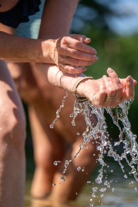 Wasser rinnt von den Händen einer Frau, die im Sommer in einem Badesee steht.