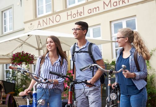 Eine Gruppe, zwei Frauen und ein Mann, stehen mit ihren Fahrrädern vor einem historischen Hotel in Glückstadt.