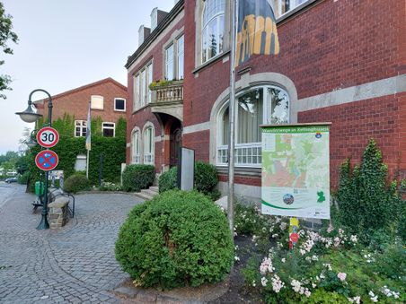 Ein rotes Backsteingebäude in Kellinghusen mit einer Karte der Wanderwege. Verkehrsschilder zeigen Tempo 30 und Halteverbot an.