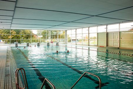 Ein Hallenbad mit großen Fenstern und mehreren Schwimmern im Wasser. Die Umgebung wirkt ruhig und einladend.