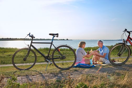 Paar ist auf Fahrrädern an der Elbe unterwegs und macht auf dem Deich eine Pause mit Picknick.