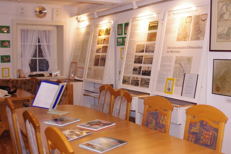 Gemütlicher Ausstellungsraum mit historischen Tafeln zu Nordfriesland und den holsteinischen Elbmarschen, Tischen, Stühlen und Broschüren.