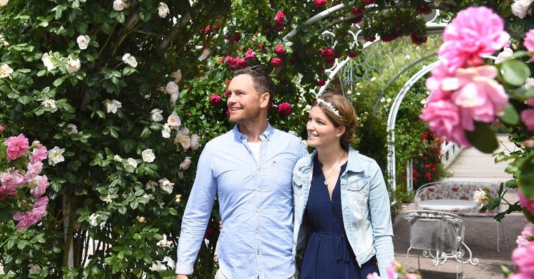 Paar im Rosarium Uetersen spaziert zwischen blühenden Rosen und einem weißen Rosenbogen.