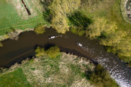 Luftaufnahme der Kanufahrt auf der Treene: Zwei Kanus fahren durch einen schmalen Flusslauf zwischen grünen Ufern und Bäumen.