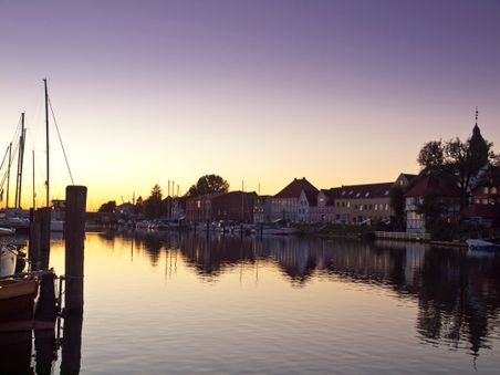Stimmungsvolle Abendstimmung im Binnenhafen mit Segelbooten und historischen Gebäuden im Hintergrund, die sich im Wasser spiegeln.