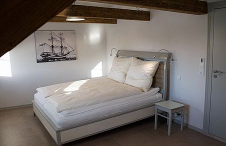 Helles Schlafzimmer mit Doppelbett, Holzbalken und Segelschiff-Bild an der Wand.