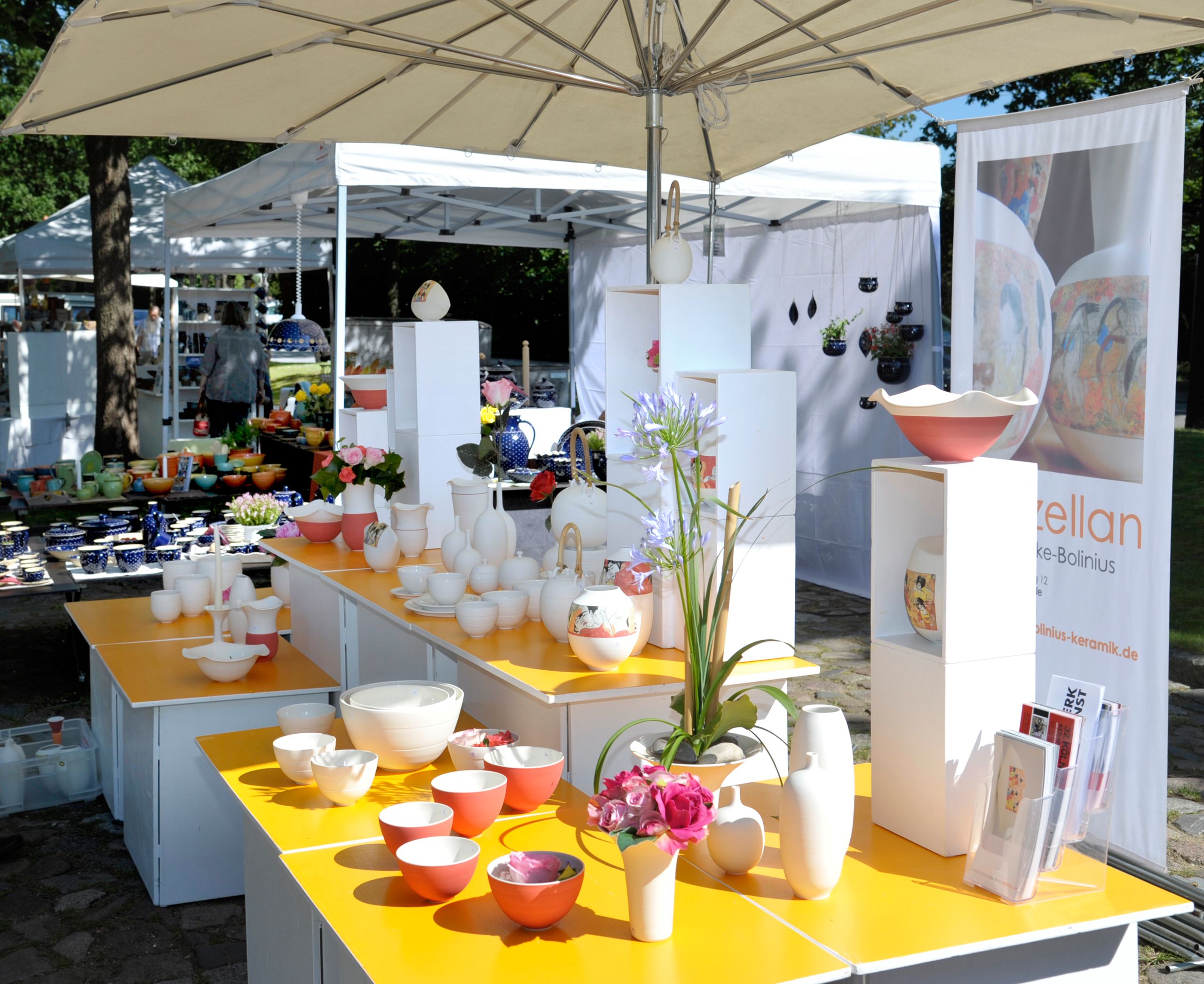 Keramikstand auf dem Töpfermarkt Kellinghusen mit farbigen Schalen, Vasen und Deko unter weißen Pavillons.