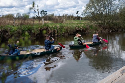 Kanufahrt Treene: Zwei Kanus mit vier Personen auf ruhigem Fluss, umgeben von Wiesen und Bäumen.