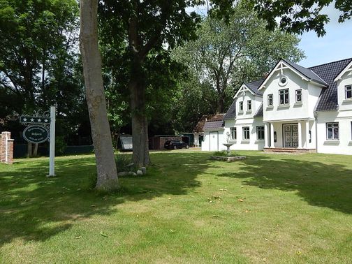 Ein elegantes, weißes Haus mit gepflegtem Garten und einem Schild mit der Aufschrift 'Bekperle'.
