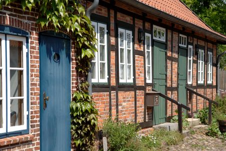 Ein charmantes Fachwerkhaus mit blauer und grüner Tür, umgeben von Kletterpflanzen und einem kleinen Garten.