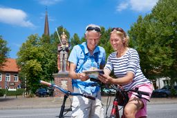 Ein Paar steht mit Fahrrädern vor der Roland-Statue in Wedel und plant mit Hilfe einer Karte die weitere Route.