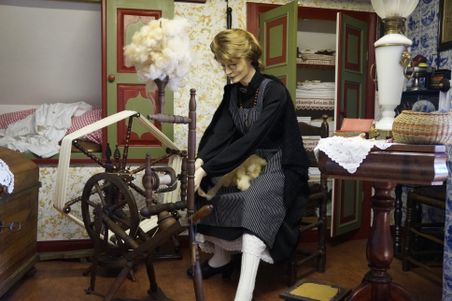 Eine Puppe am alten Webstuhl im Dorfmuseum Ottenbüttel, umgeben von historischen Möbeln und Textilien.