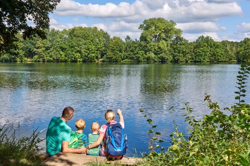 Familie am Rensinger See bei Kellinghusen in Holstein blickt über das Wasser auf das bewaldete Ufer.