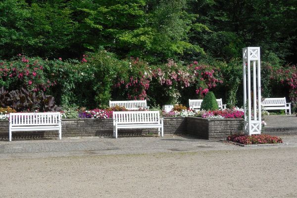 Rosengarten Pinneberg mit Nachbauten der Möblierung von 1935: weiße Bänke, Blumenbeete und Rankhilfe vor dichtem Grün.
