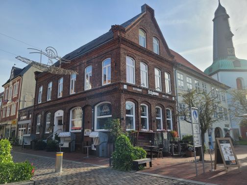 Außenansicht von „Stilbruch“: Backsteingebäude mit Restaurant, Hotel und Café neben einer Kirche mit Turm.