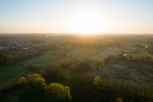 Luftaufnahme der Wedeler Au und Wedel in Holstein bei Sonnenuntergang über Wiesen, Bäumen und einer Siedlung.