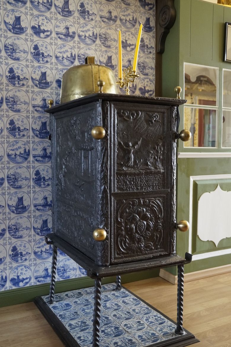 Historischer Ofen im Dofmuseum Ottenbüttel mit blau-weißem Kachelmuster, Messingaufsatz und Kerzenhalter.