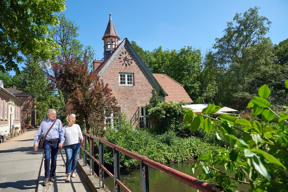 Ein Ehepaar spaziert über die Brücke zur Schlossinsel im Rantzauer See in Barmstedt. Im Hintergrund steht das Schlossgefängnis.