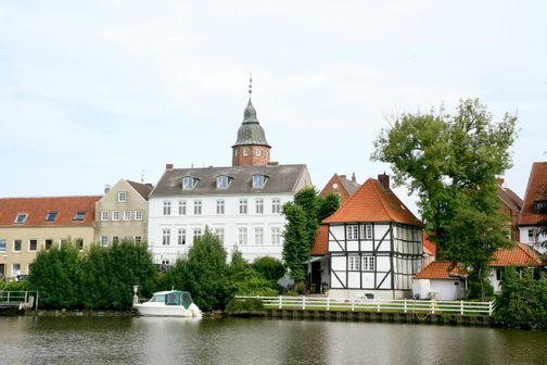 Historische Häuser in Glückstadt an einem Kanal, mit Kirchturm und Boot am Ufer.
