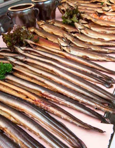 Eine Theke mit zahlreichen geräucherten Fischen, vor allem Aalen, dekoriert mit Kräutern und Keramikbechern.