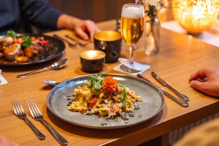 Ein stilvoll gedeckter Tisch in einem Restaurant mit einem Teller Pasta, garniert mit einer Blume. Ein Glas Bier steht daneben.