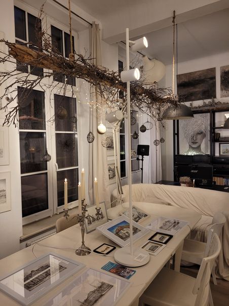 Atelier Lamade: heller Kunstraum mit hängendem Ast, Lichterketten, Kerzen und gerahmten Zeichnungen auf einem Tisch.