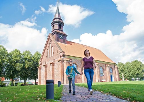 Frau und Kind vor der Jakobuskirche in Brunsbüttel, Holstein, bei sonnigem Wetter.