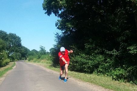 Straßenboßeln Burg: Ein Mann in rotem Shirt wirft auf einer ländlichen Straße eine Boßelkugel.