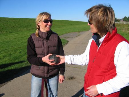 Zwei Frauen stehen auf einem Weg im Grünen und übergeben eine Bosselkugel.