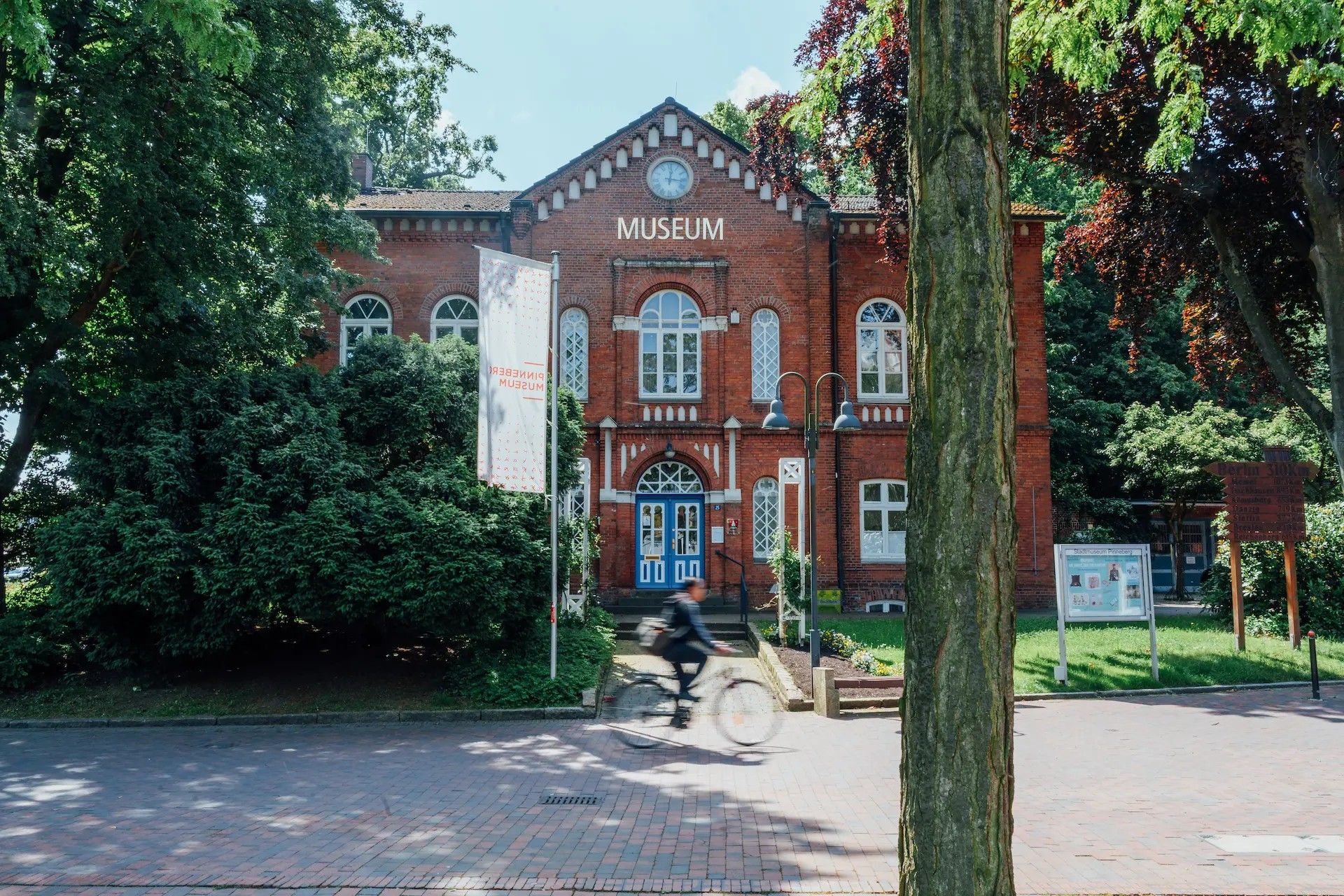 Ein rotes Backsteingebäude mit der Aufschrift 'Museum'. Ein Radfahrer fährt schnell vorbei. 