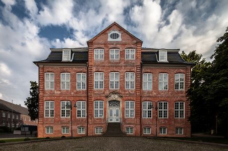 Historisches Backsteingebäude mit symmetrischer Fassade, zentraler Treppe und dramatischem Wolkenhimmel.