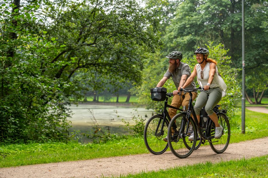 Paar genießt eine Fahrradtour im Grünen und fährt durch den Kurpark in Bad Bramstedt.